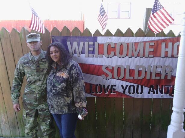 A US military soldier poses in front of a custom welcome home banner